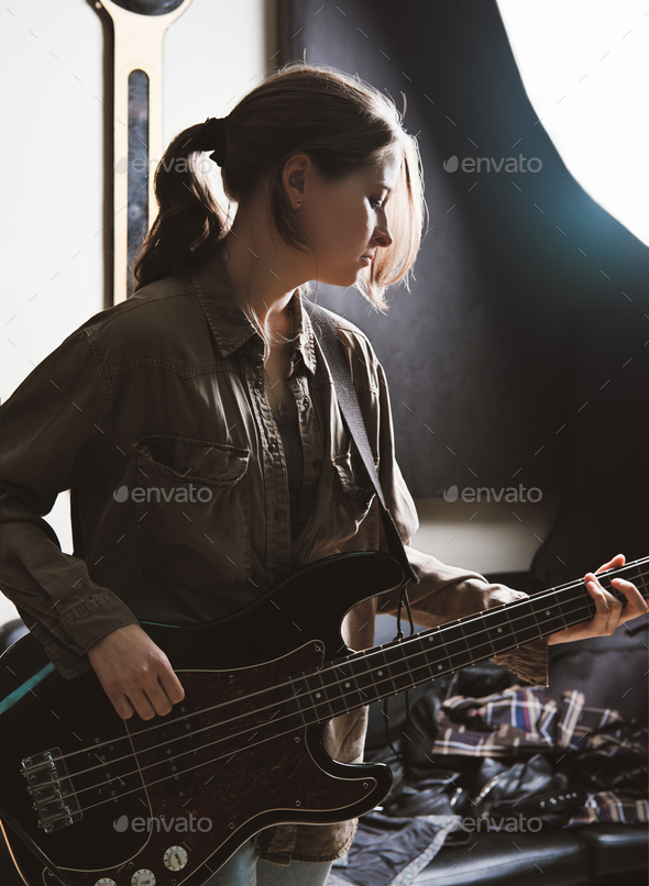 young woman playing electric bass guitar in a studio. rock musician rehearsal room.