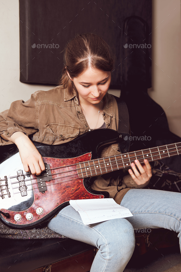 young woman playing bass guitar and looking at chords notes. rehearsal room. female rock musician