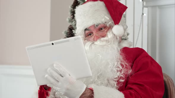 Joyful Santa Claus Checking Up Christmas Emails From Children on His Digital Tablet alt