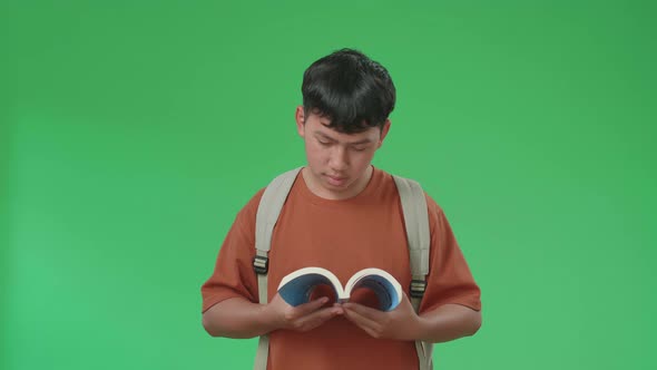 The Front View Of Asian Boy Student Reading A Book While Walking On Green Screen alt