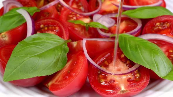 Tomato salad with basil and chopped onion poured oil in white ceramic dish rotate slowly.