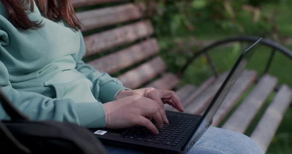 Woman's Fingers Are Typing On Laptop She Is Sitting On Bench In City Park