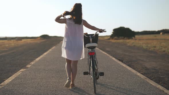 Back View Portrait of Slim Young Caucasian Woman Strolling with Bicycle at Cyprus Landscape alt