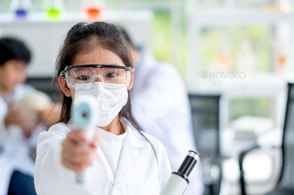 Little girl with hygiene mask and protective eye glasses show infrared thermometer