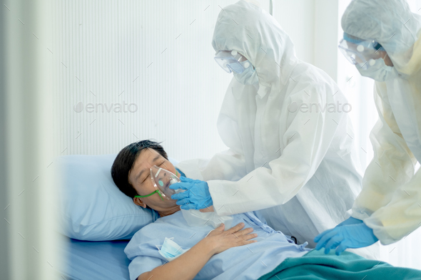 Nurse or hospital staff with full body cover suit help to put aspirator mask to Covid-19 patient