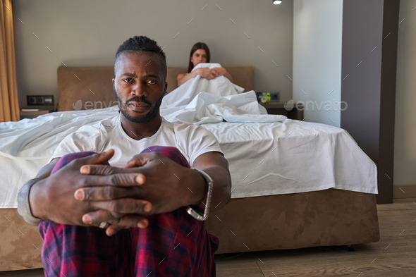 Low-spirited young man and female sitting apart in bedroom