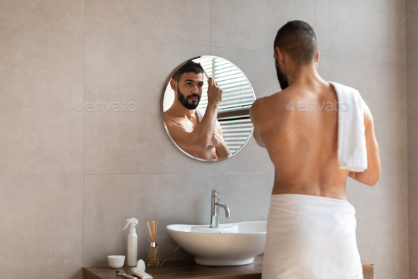 Back rear view of guy looking in mirror brushing hair - Stock Photo - Images