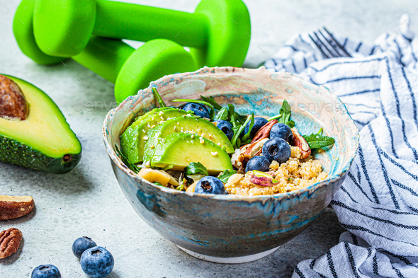 Quinoa salad with berries, avocado and nuts, dumbbells on the background. Healthy post-workout food.