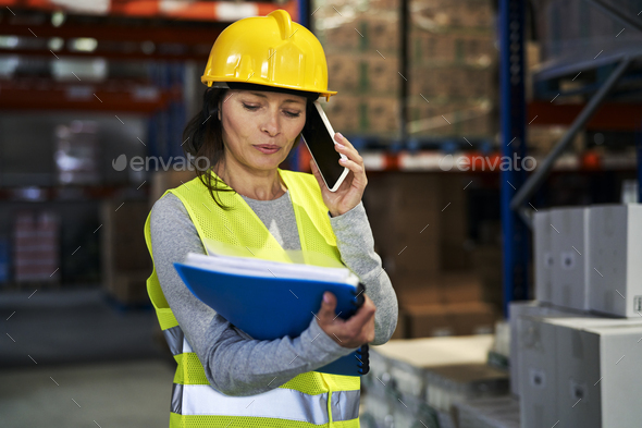 Adult caucasian woman talking by mobile phone in warehouse - Stock Photo - Images