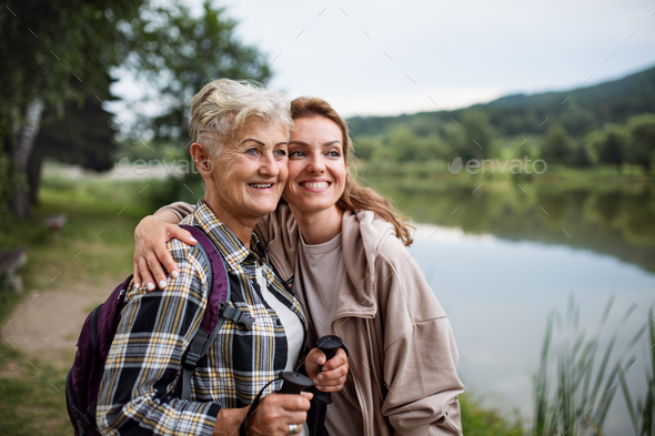 Happy senior mother hiker embracing with adult daughter by lake outdoors in nature - Stock Photo - Images