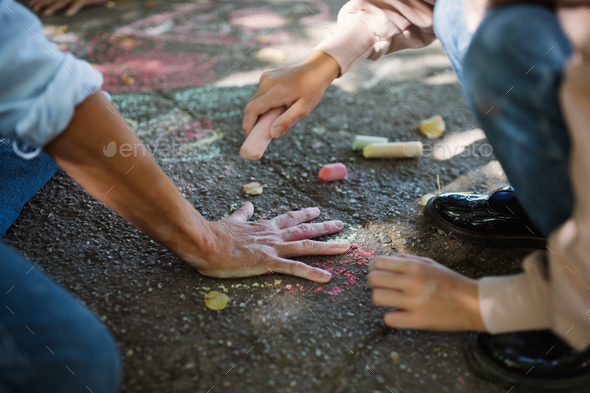 Unrecognizable little girl drawing grandmother's hand with chalk on pavement outdoors - Stock Photo - Images