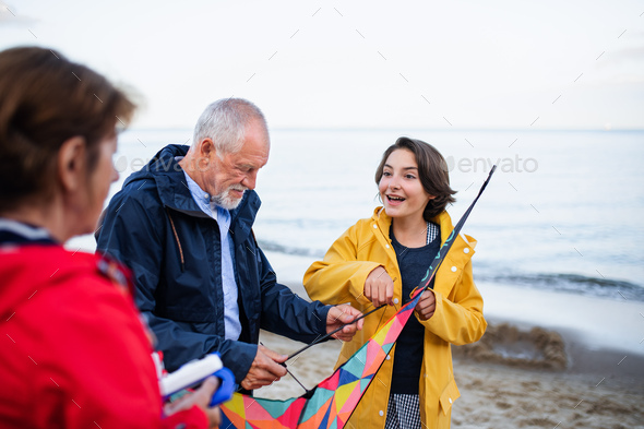 Grandparents with preteen girl preparing kite for flying on sandy beach - Stock Photo - Images