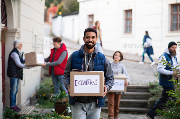 Happy young volunteer with team delivering donation boxes and looking at camera, social care concept - Stock Photo - Images