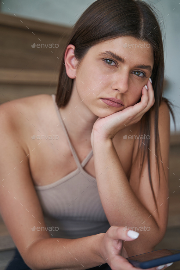 Low-spirited young woman with cellphone staring ahead