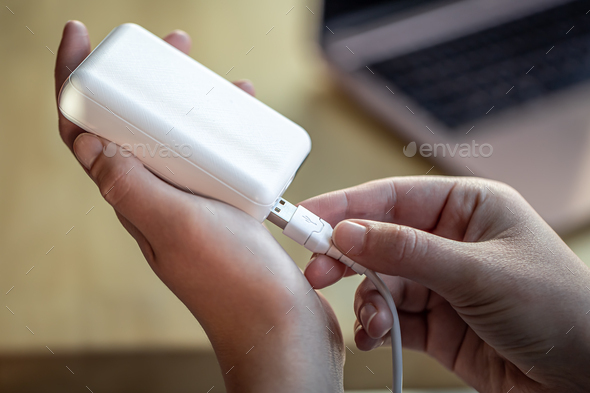 Woman\'s hand holding white USB cable and white power bank.