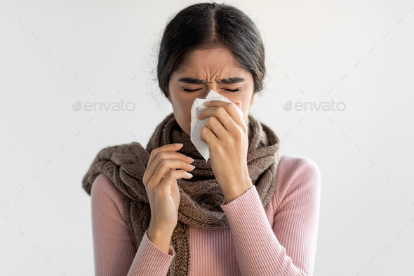 Portrait of sad upset young indian woman in scarf blows her nose and wipes nose with tissue
