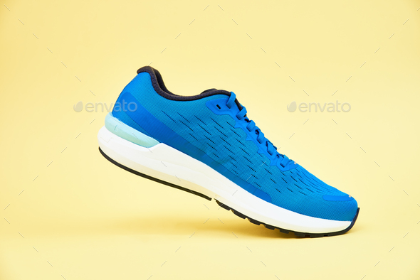 Blue running sneaker on yellow background, close up