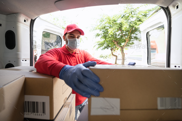 Young delivery man loading boxes in van truck while wearing face mask and gloves
