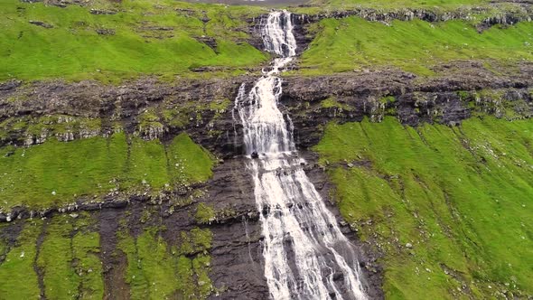 Aerial view of breathtaking waterfall crossing rock mountain, Faroe Island. alt