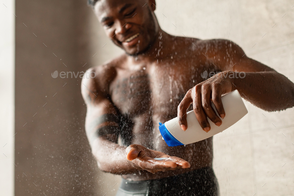 Handsome Black Guy Taking Shower Squeezing Shampoo Bottle In Bathroom