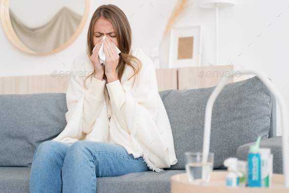 Coronavirus. Ill young woman blowing nose, coughing or sneezing in tissue, suffering from flu