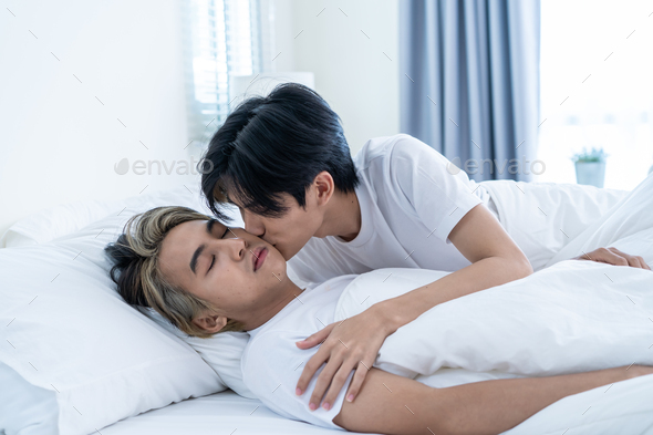 Asian attractive gay kiss boyfriend\'s forehead to wake up from sleep.