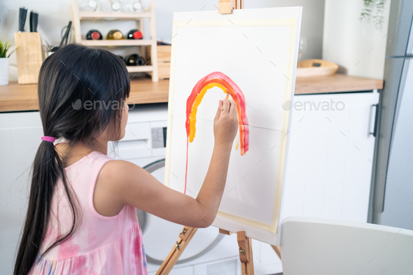 Asian young happy kid girl coloring on painting board in living room.