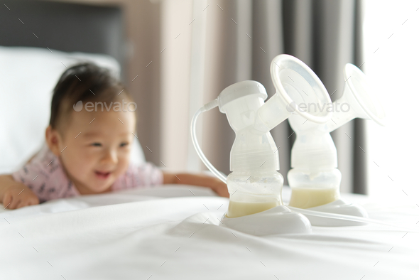 Breast milk in milk pump\'s bottles on the bed with smiling baby crawling in background.