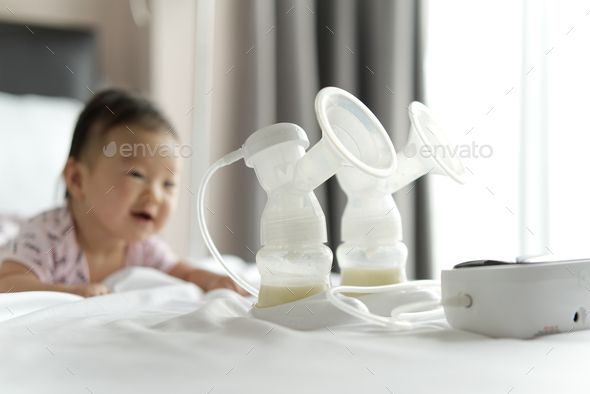 Breast milk in milk pump\'s bottles and pump machine on the bed.