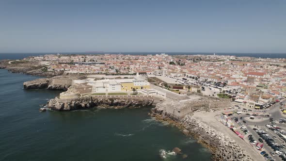 Aerial pullback shows Peniche Fortess on coast, famous landmark; Portugal