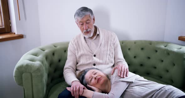 an Elderly Woman Lies on Her Old Husband's Lap in a Cozy Country House alt