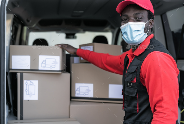 African delivery man loading boxes in van truck while wearing face mask to avoid corona virus spread