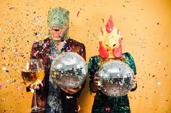 Crazy couple having fun holding disco balls and champagne glass at party - Focus on chicken mask