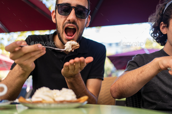 Man with the mouth opened ready to eat a portion of a crepe with cream