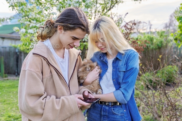 Teenagers with decorative rabbit in hands talking and looking at smartphone