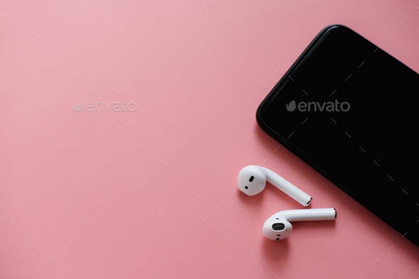 White wireless bluetooth earphones on pink background. headphones and smartphone with copy space