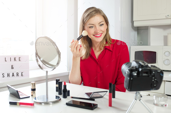 Cheerful young woman shows her brush for make up recording beauty video blog