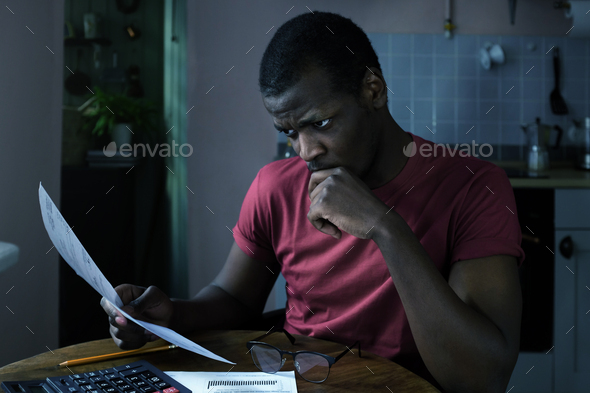Angry young african man looks at bills to pay lying his hand, facing unpaid debt troubles