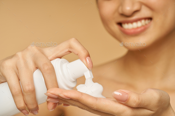 Cropped shot of young woman smiling, holding a bottle of gentle foam facial cleanser isolated over