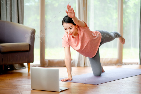 Beautiful women doing yoga by stretching leg and arm and look example from laptop