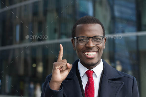 Young african businessman in glasses keeps finger pointed upwards showing something