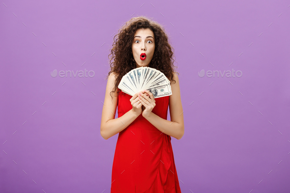Studio shot of woman being lucky in casino winning lots of cash holding money in hands saying wow