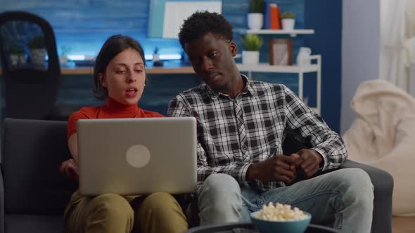 Interracial Couple Looking at Laptop and Sitting on Sofa alt