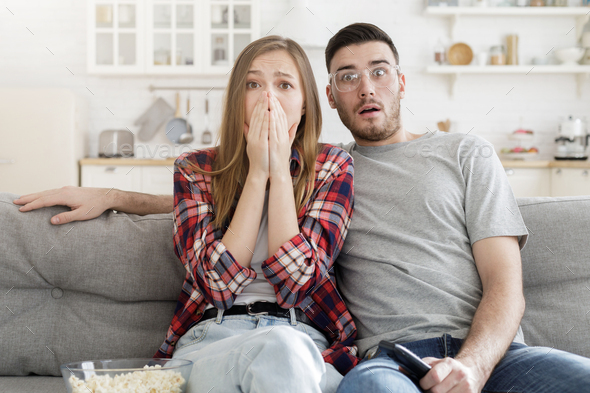 Really frightened couple watching horror film at home sharing thoughts