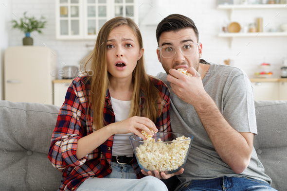 Excited young family watches TV channel sitting on couch at home with popcorn
