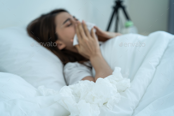 Asian sick girl in pajamas wake up from sleep at night sneezing on bed.