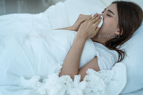 Asian sick girl in pajamas wake up from sleep at night sneezing on bed.