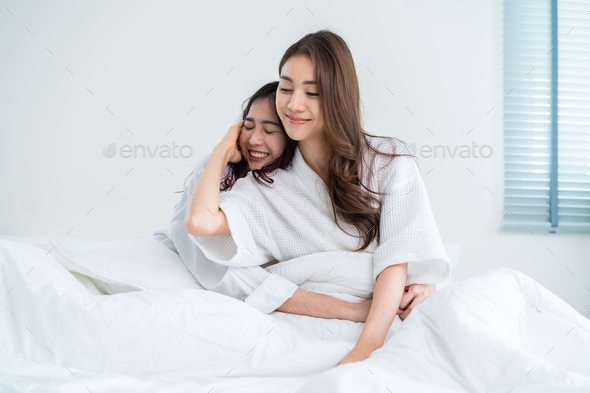 Portrait of Asian young lesbian couple sit on bed and hug each other.