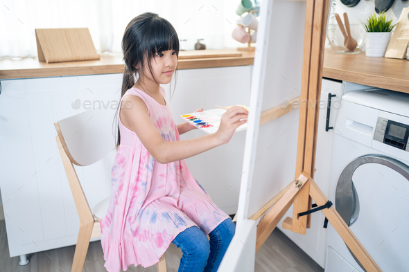 Asian young happy kid girl coloring on painting board in living room.