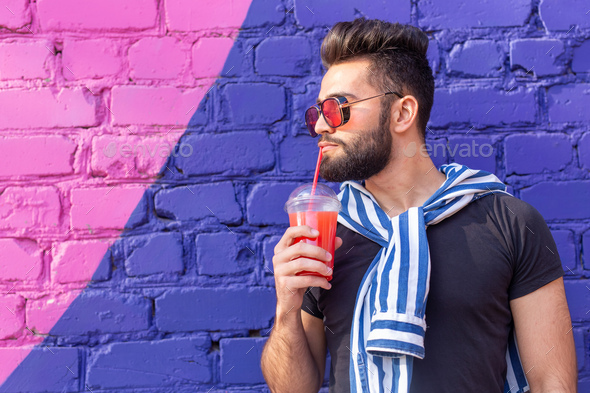 Portrait of a positive cheerful young arab man with a glass of juice ...